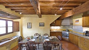 Une cuisine rustique avec des poutres en bois, une table à manger dressée pour quatre personnes et un grand poêle.