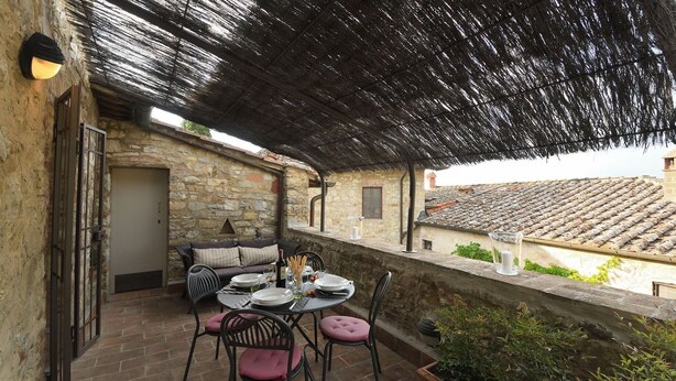 An outdoor patio with stone walls, a thatched roof, a table set for dining, and a view of terracotta rooftops. - Pergola, Montebuoni, Gaiole in Chianti, Siena and Chianti (Gaiole in Chianti)