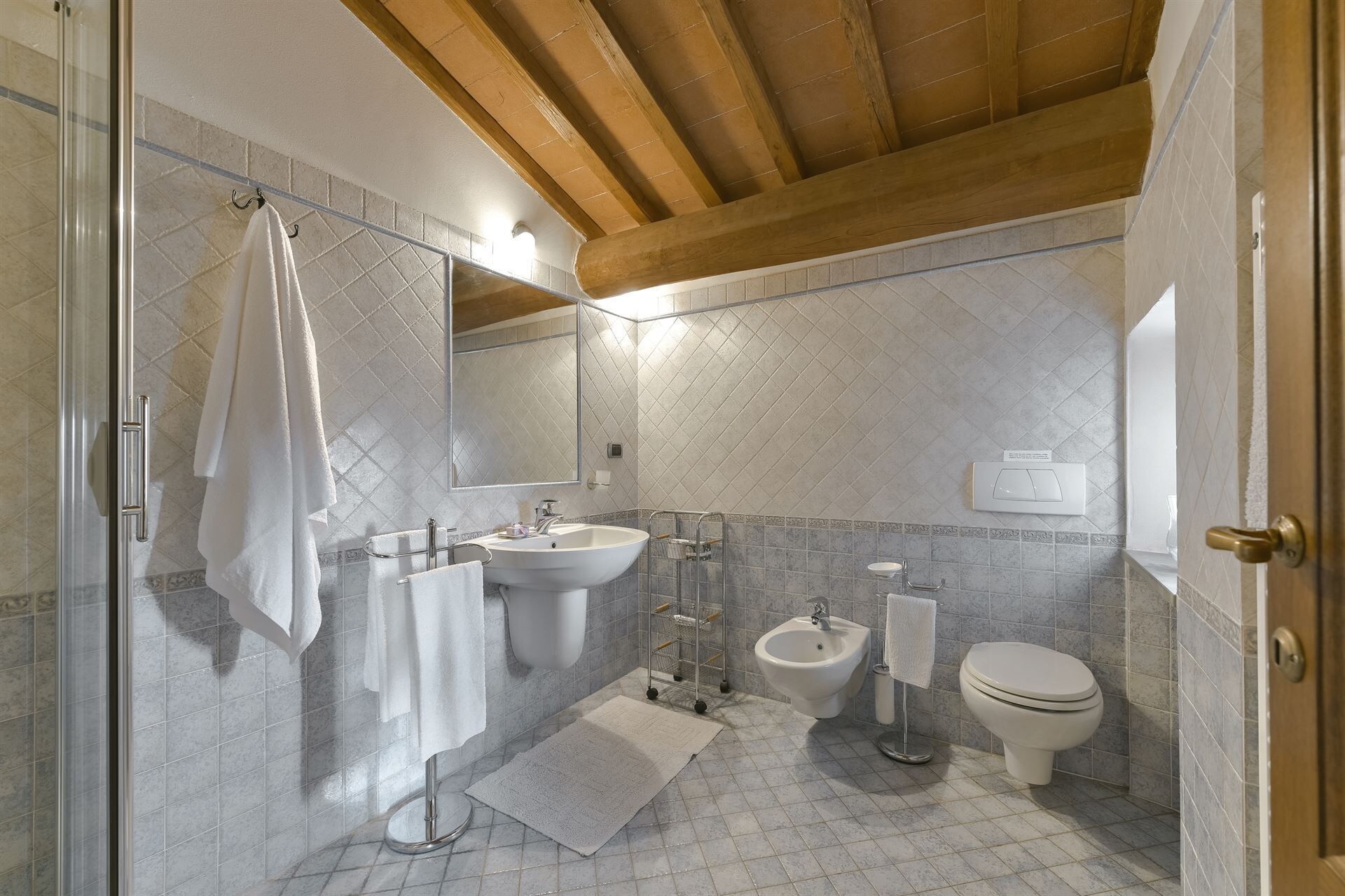 A bathroom with a shower, sink, bidet, toilet, and a towel rack.