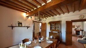 A dining area with a wooden table set for four, surrounded by chairs. A chandelier hangs from the ceiling, and there are shelves with candles and a framed picture on the wall. - Mastro 3, San Sano, Gaiole in Chianti, Siena and Chianti (Gaiole in Chianti)