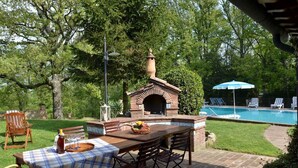 An outdoor patio with a brick pizza oven, a pool, and lounge chairs.