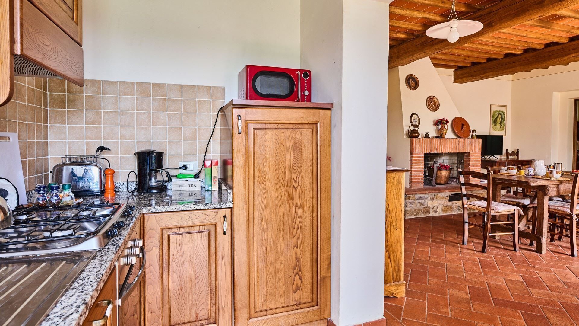 A kitchen with a gas stove, a microwave, and a coffee maker. There is a wooden cabinet and a tiled backsplash.