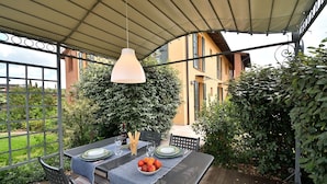 An outdoor patio with a table set for dining, surrounded by greenery and a covered area.