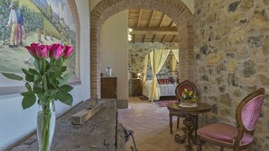 A rustic room with a stone wall, a wooden table with a chair, a bed with a canopy, and a painting of a vineyard scene. - Villa di Capannole 12, Bucine, Arezzo and Cortona (Bucine)