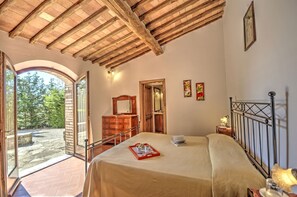 A bedroom with a bed, a dresser, a mirror, and a window overlooking a garden. - La Querce, Rocca di Castellina, Castellina in Chianti, Siena and Chianti (Castellina in Chianti)