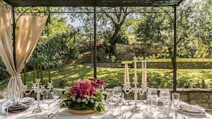 Un área de comedor al aire libre con una mesa dispuesta para una comida, rodeada de follaje y un muro de piedra.