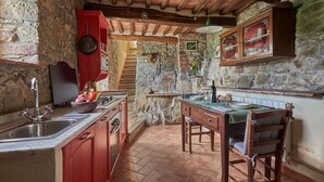 A rustic kitchen with stone walls, wooden beams, a red cabinet, and a dining area with a table set for two. - La Roccia, Brandeglio, Bagni di Lucca, Lucca and Viareggio (Bagni di Lucca)