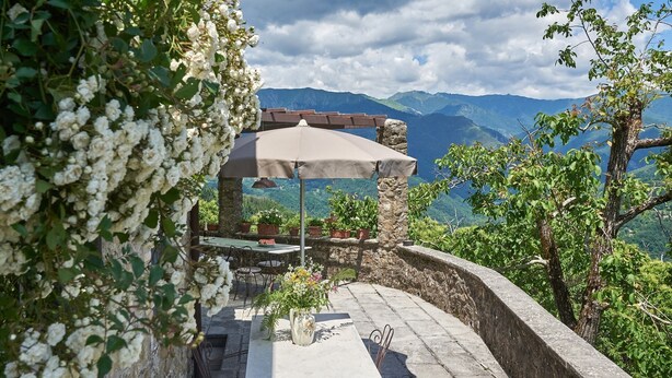 A stone patio with a table and chairs, a pergola with an umbrella, and a view of mountains. - La Roccia, Brandeglio, Bagni di Lucca, Lucca and Viareggio (Bagni di Lucca)