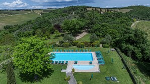 Ein großer rechteckiger Pool, umgeben von Rasen und Bäumen, mit einem Weg zu einem Gebäude.