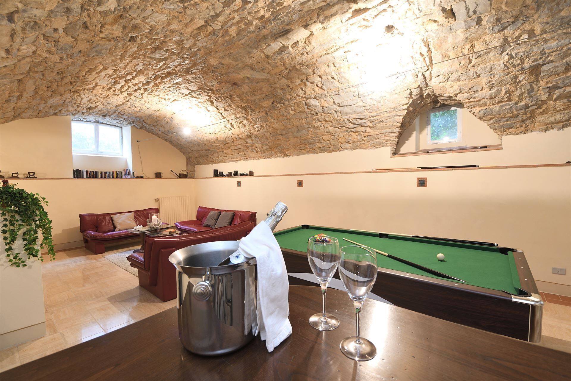 A cozy room with a pool table, a leather sofa, and a dining table with a metal bucket and glasses.