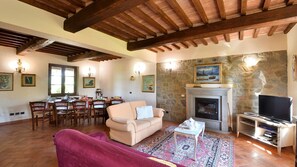 A cozy living room with a fireplace, wooden beams, stone wall, and a television.