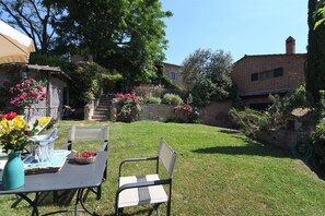 A backyard with a table set for dining, a chair, and a basket of fruit.
