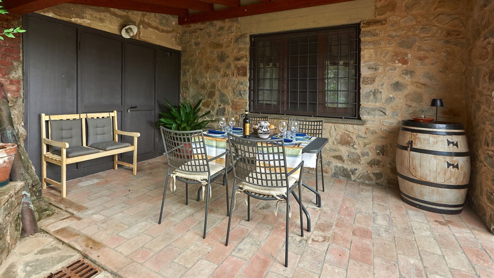 Eine Terrasse mit Steinmauern, an einem Tisch für vier Personen, zwei Stühle, eine Bank und einem Holzbottich.