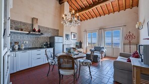 A spacious kitchen with white cabinets, a dining area with a round table, and a view through large windows. - Scorpione, Montefiorile, Gaiole in Chianti, Siena and Chianti (Gaiole in Chianti)