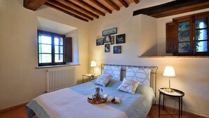 A bedroom with a bed, two bedside tables, a window, and a radiator.