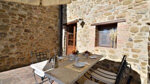 A stone-walled outdoor dining area with a table set for two, metal chairs, and a window with a view.