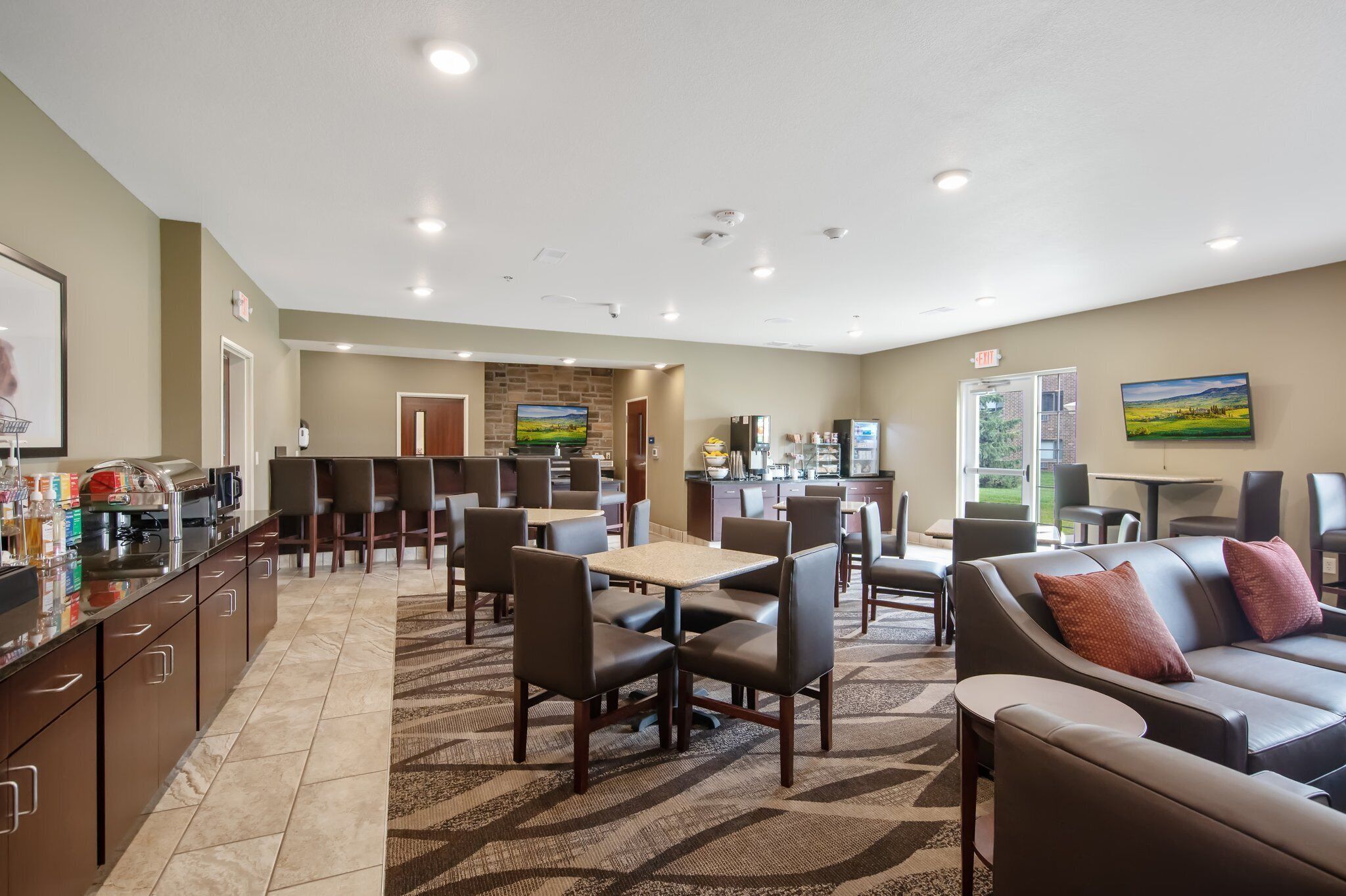 A hotel lobby with a dining area, kitchen, and a large window with a view of the outdoors.