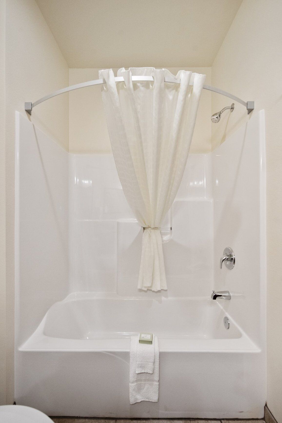 Una vasca da bagno bianca con tenda da doccia legata al centro, un asciugamano appeso al lato e un rubinetto cromato.