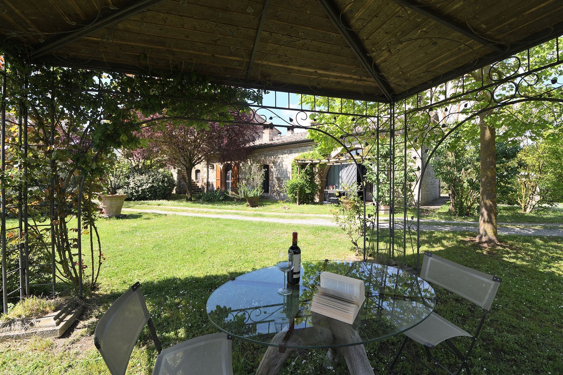 Un patio al aire libre con una mesa redonda de vidrio, una silla de metal y una botella de vino.