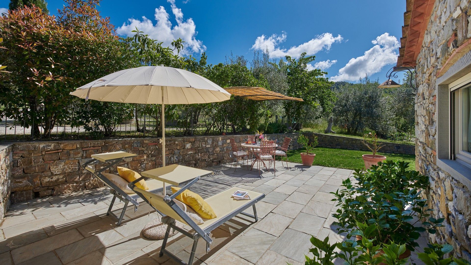 An outdoor patio with stone flooring, a lounge chair, a table, and two umbrellas.