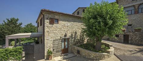 A stone building with a covered patio, a tree in the courtyard, and a gravel driveway.