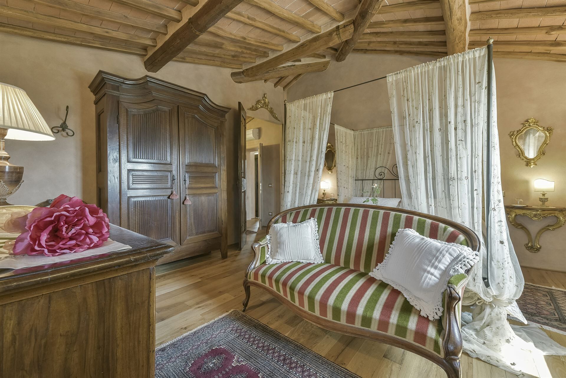 A room with a wooden ceiling, a striped sofa, a large mirror, and a wooden wardrobe.