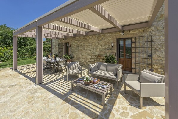 An outdoor patio with stone flooring, a pergola with striped beams, and a stone wall. - Vecchio Frantoio, Gaiole in Chianti, Siena and Chianti (Gaiole in Chianti)