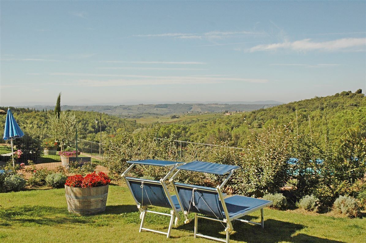 A garden with a view of rolling hills, a blue umbrella, and a chair with a solar panel.