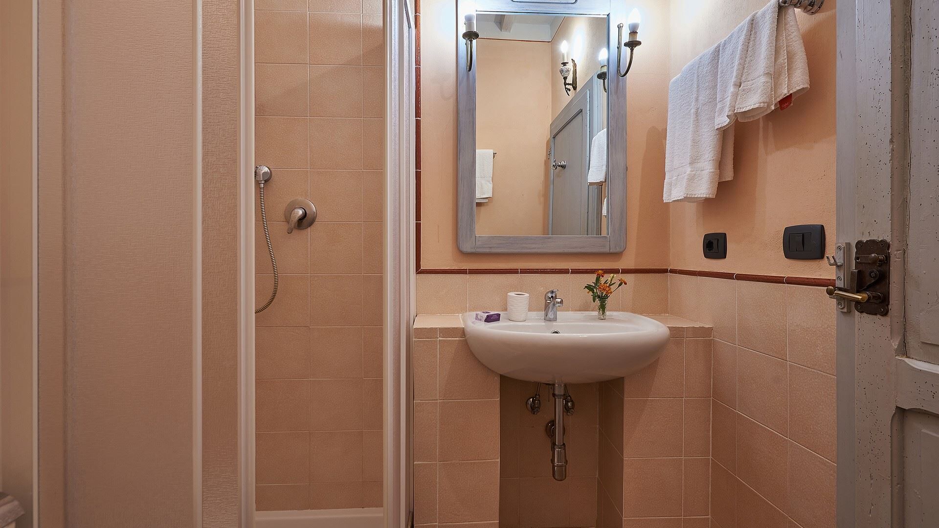 A bathroom with a glass shower enclosure, a sink with a mirror above it, and a towel hanging on the wall.