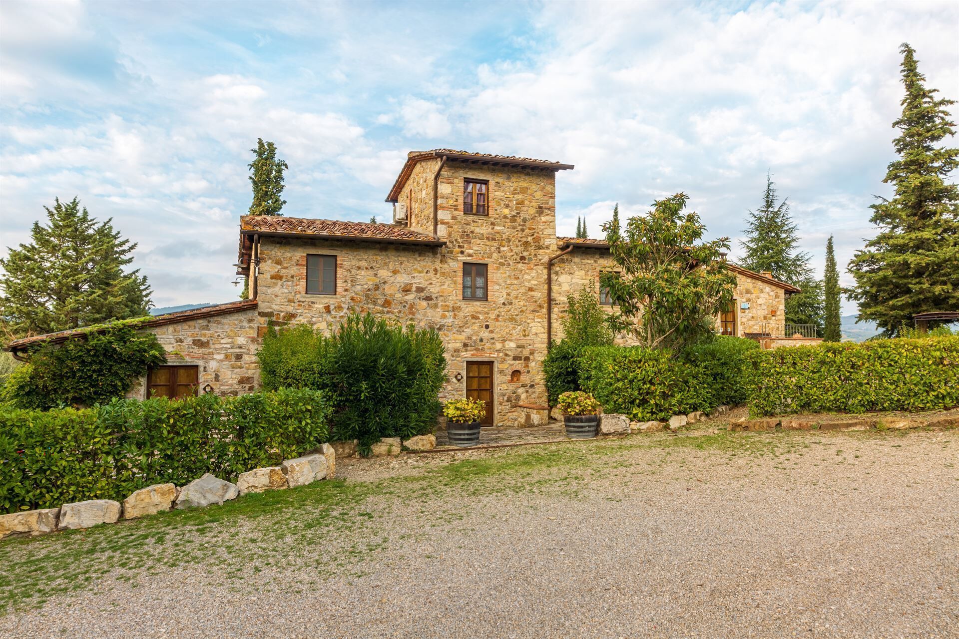 A stone building with a tiled roof, surrounded by greenery and trees.