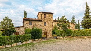 A stone building with a tiled roof, surrounded by greenery and trees.