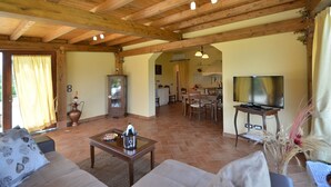 Amplia sala de estar con techo de madera, televisor, chimenea y un comedor al fondo.