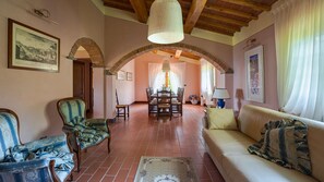 A spacious living room with a high ceiling, a dining area with a table set for four, and a sofa with decorative pillows.