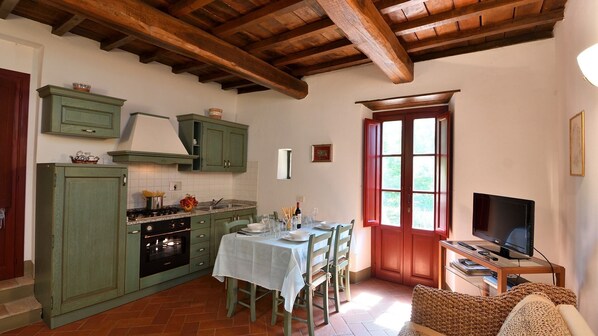 A rustic kitchen with green cabinets, a stove, and a dining area with a table set for four. - Raffaello, Montefienali, Gaiole in Chianti, Siena and Chianti (Gaiole in Chianti)