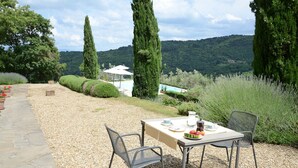 An outdoor dining area with a table set for two, surrounded by gravel, with a view of a pool and mountains in the background. - Poggetto, Greve in Chianti, Florence and Chianti (Greve in Chianti)