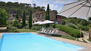 A swimming pool with lounge chairs and umbrellas, surrounded by a landscaped garden and a stone building. - Poggetto, Greve in Chianti, Florence and Chianti (Greve in Chianti)