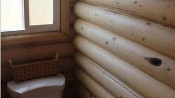 A log cabin bathroom with a toilet, a window, and a basket on the floor.