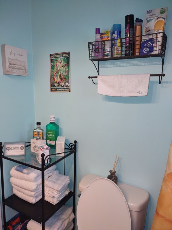 Une salle de bain comprenant des toilettes, une étagère avec des articles de toilette, un porte-serviettes et une affiche encadrée au mur.