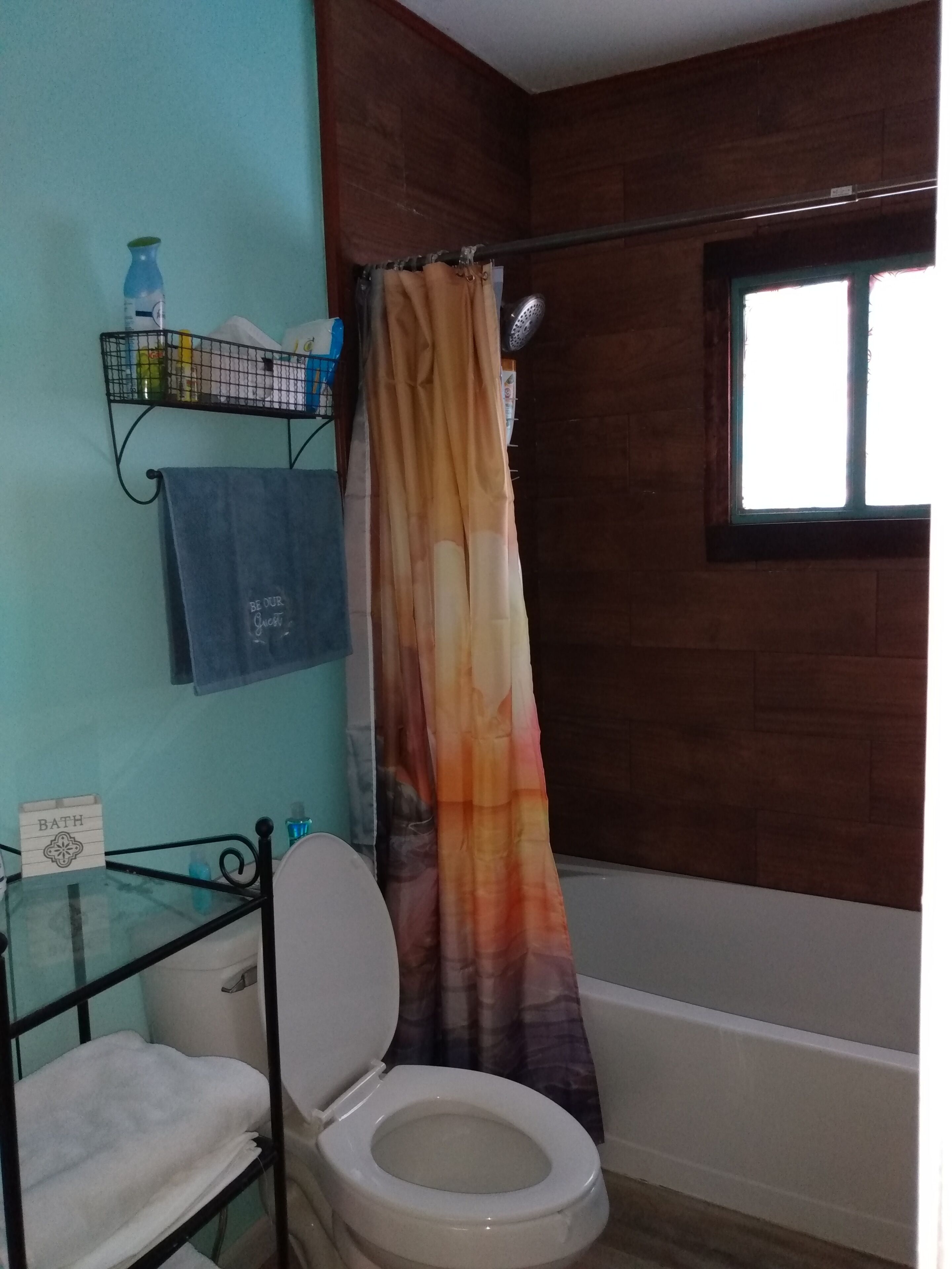 Une salle de bain avec des toilettes blanches, une étagère en verre où sont rangés les articles de toilette, une serviette bleue et un rideau de douche.