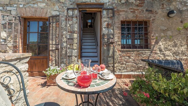 A stone building with a wooden door, a staircase, and a table with a pitcher, glasses, and fruit. - Bella Vista, Montebuoni, Gaiole in Chianti, Siena and Chianti (Gaiole in Chianti)