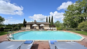 Una piscina con lettini e ombrelloni, circondata da un edificio in pietra con tetto in tegole.