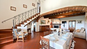 Un'ampia zona giorno con tavolo da pranzo apparecchiato, una scala con ringhiera in ferro battuto e un camino.