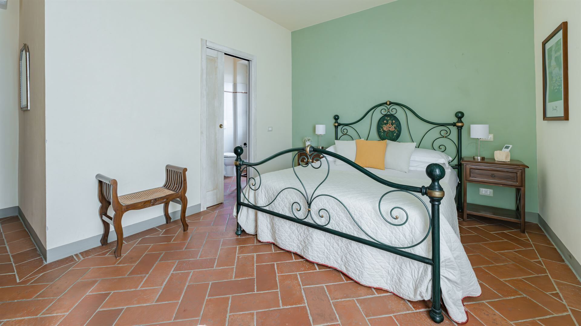 A bedroom with a bed, a nightstand, a chair, and a door leading to another room.