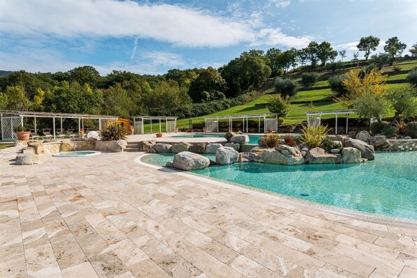 A pool area with stone tiles, rock landscaping, and a pergola structure.