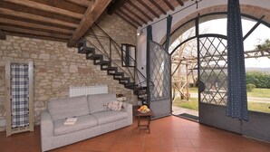 A room with a stone wall, a grey sofa, a wooden staircase, and a large arched window. - Limonaia, Palazzo a Merse, Sovicille, Siena and Chianti (Sovicille)