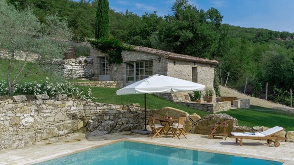 A stone house with a pool, outdoor furniture, and a white umbrella.