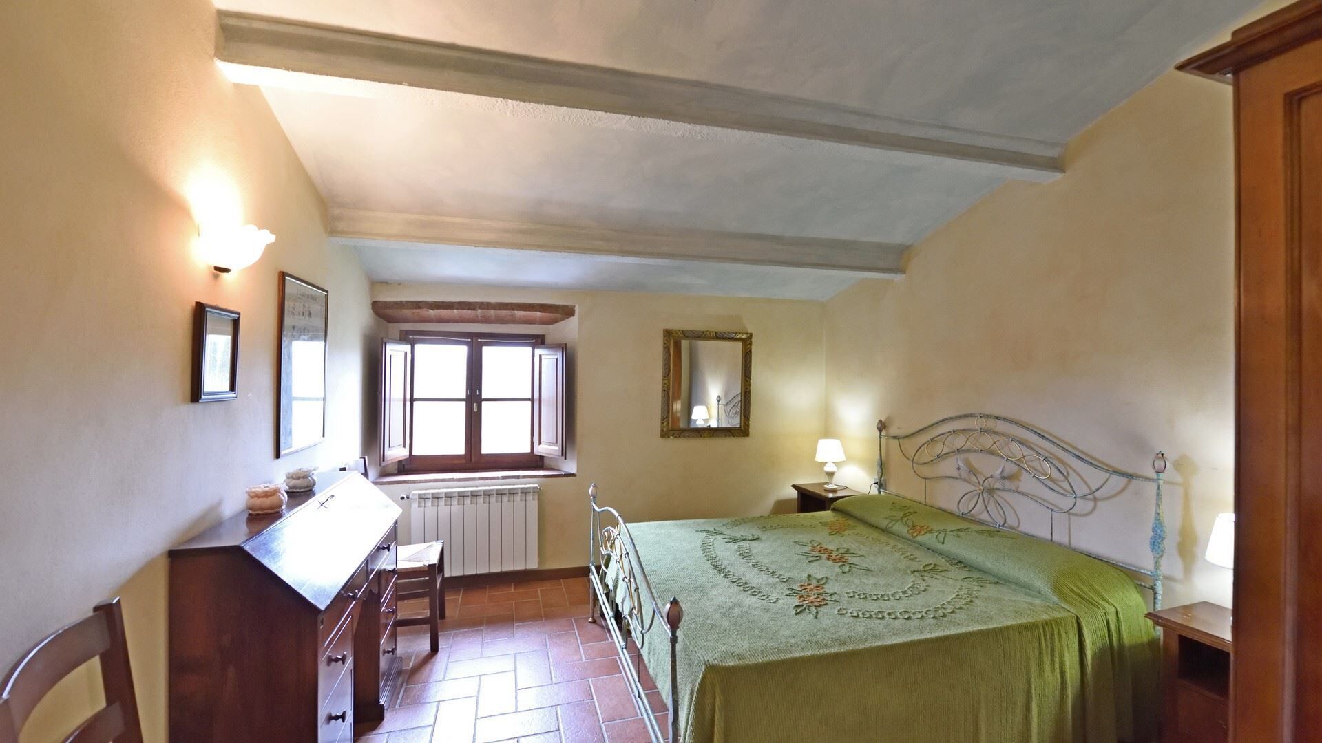 Ein Schlafzimmer mit Bett, Schreibtisch, Stuhl, Fenster und Heizkörper.