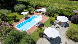 Een rechthoekig zwembad met een jacuzzi, omringd door een terras met buitenmeubilair en parasols.