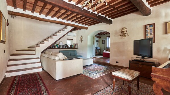 Amplia sala de estar con escalera, sofá, televisor y piano.