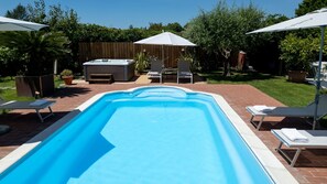 A rectangular swimming pool with a brick border, surrounded by lounge chairs and umbrellas.
